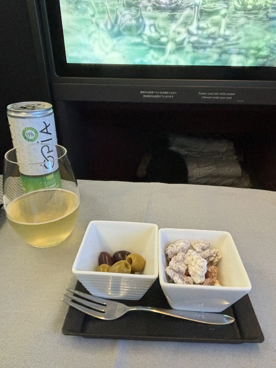 JL12ビジネスクラスの最初の飲み物。ノンアルコールのスパークリングの缶とグラス、オリーブとナッツの小鉢