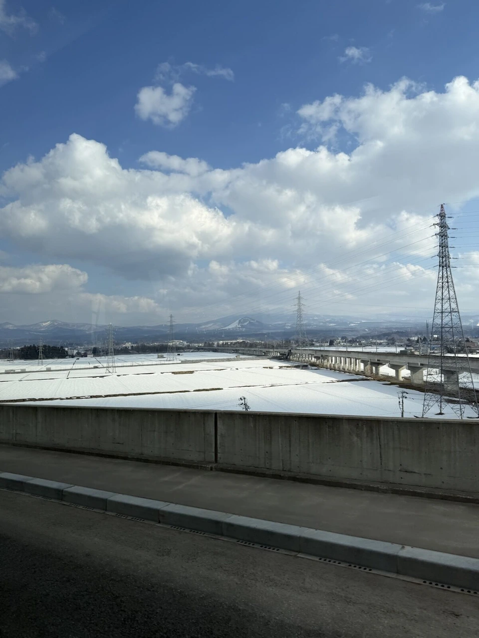 青森空港の近くの道から見た、雪に覆われた畑と鉄塔、青空と白い雲