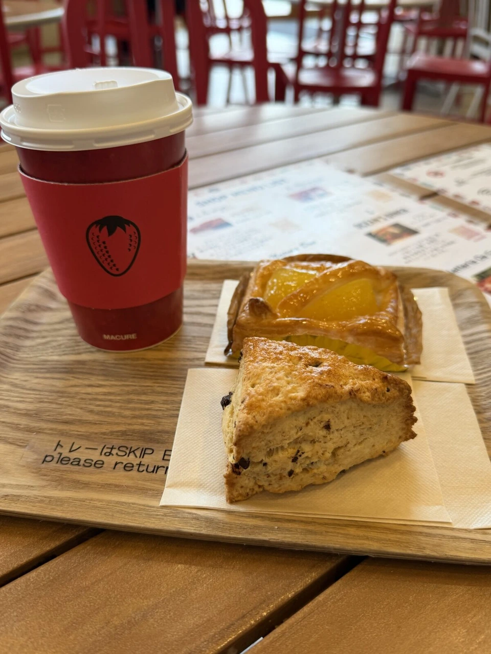 木のテーブルに置いた赤いカップのコーヒーと、りんごがのったパイとスコーン