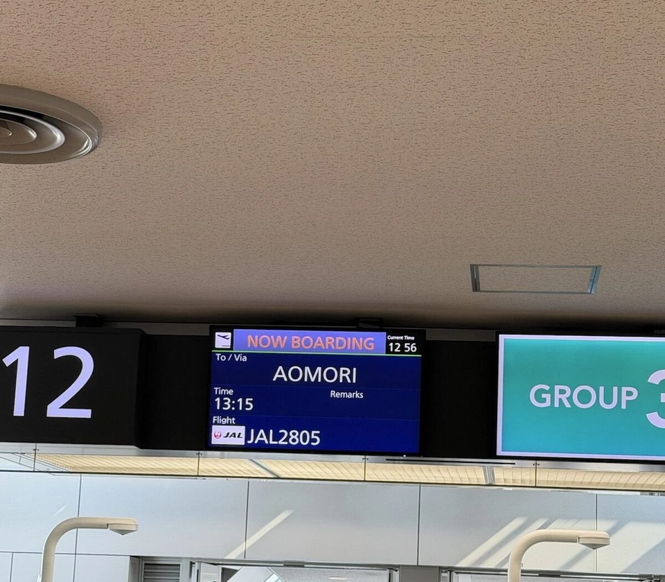 新千歳空港の12番搭乗口の表示。NOW BOARDINGの文字、行き先AOMORI、JAL2805、横にGROUP 3の看板