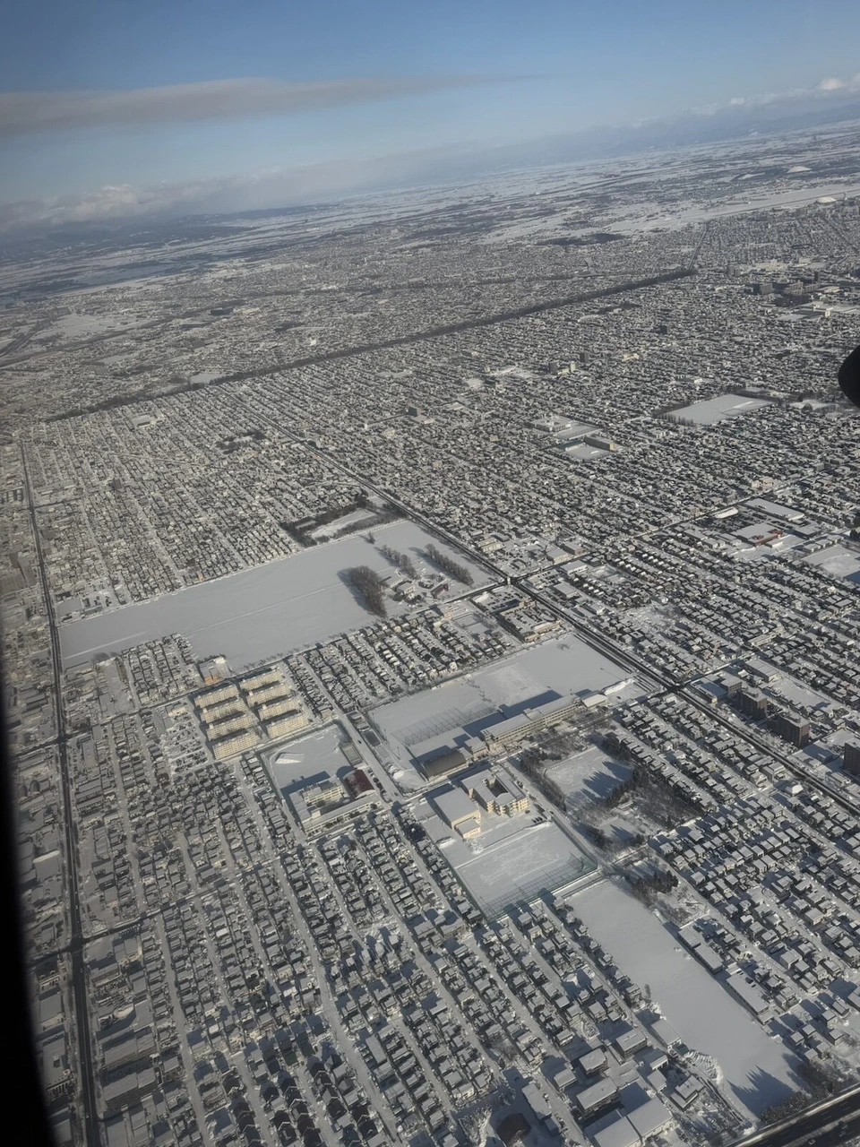 丘珠空港への着陸前、JL2824の機窓から見た雪の札幌の住宅街と学校のグラウンド