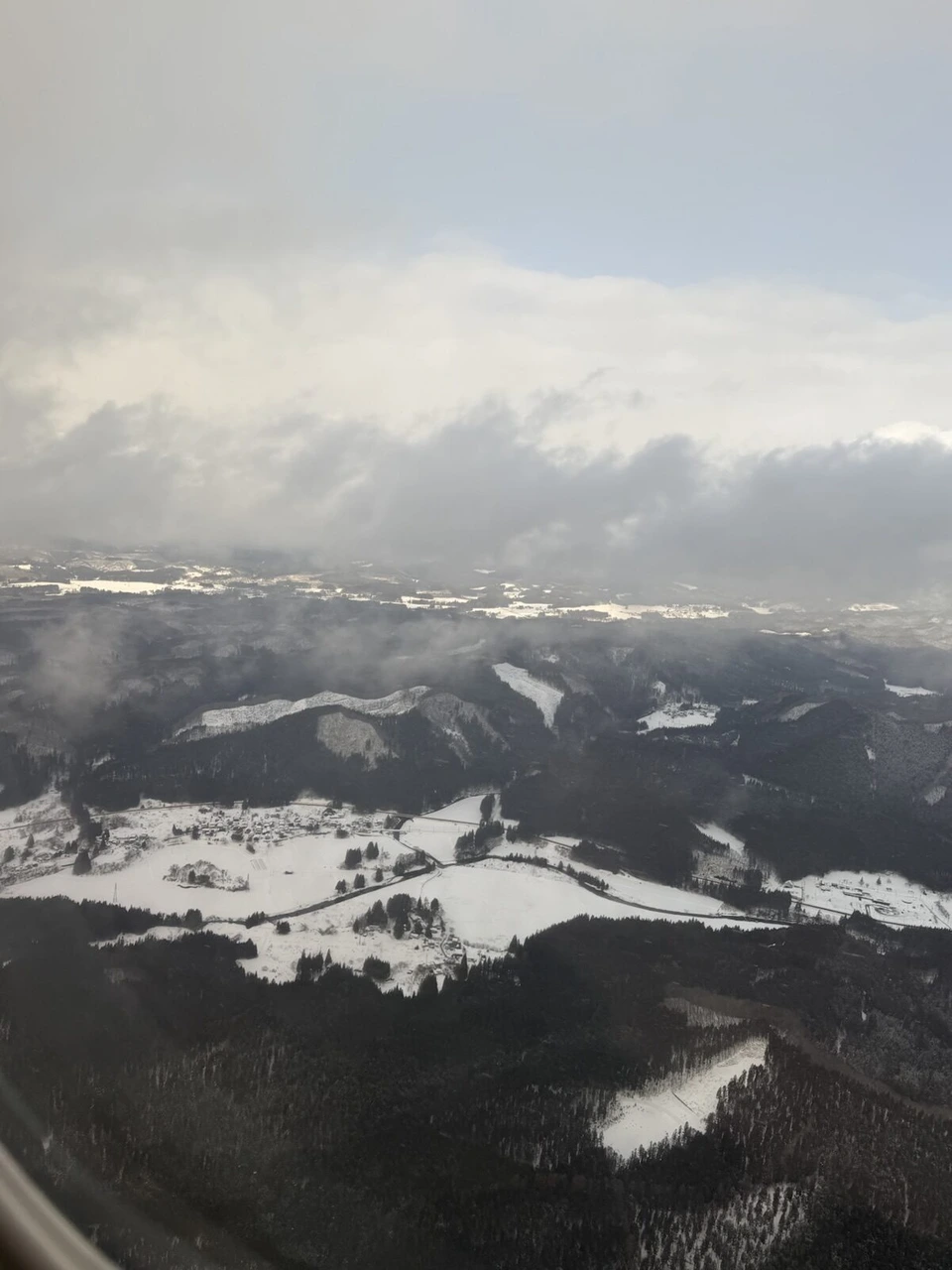 JL163で秋田空港に近づく機窓。雪に覆われた田畑と集落、低い雲