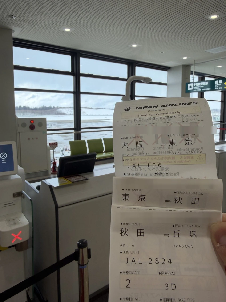 秋田空港の2番搭乗口で手に持った3枚の搭乗案内。大阪→東京のJAL106、東京→秋田、秋田→丘珠のJAL2824で座席は3D。奥の窓の外は雪景色
