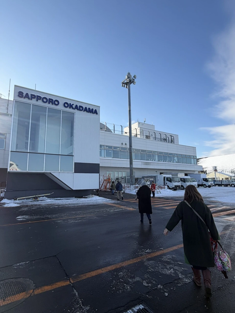 丘珠空港のターミナル。SAPPORO OKADAMAの文字、駐機場を歩いてターミナルへ向かう乗客の後ろ姿