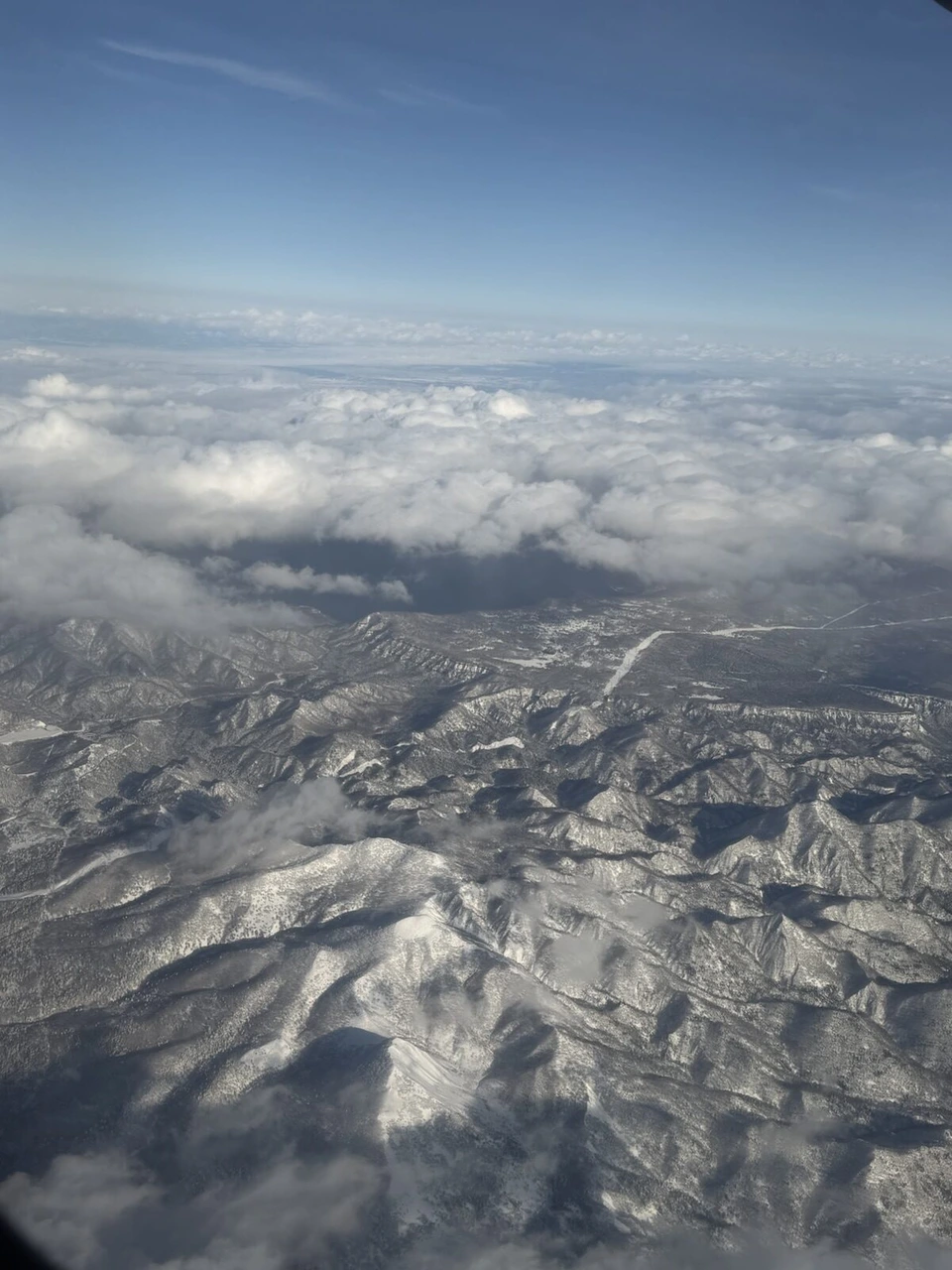 JL2824の機窓から見た北海道の雪山と、その上に広がる雲