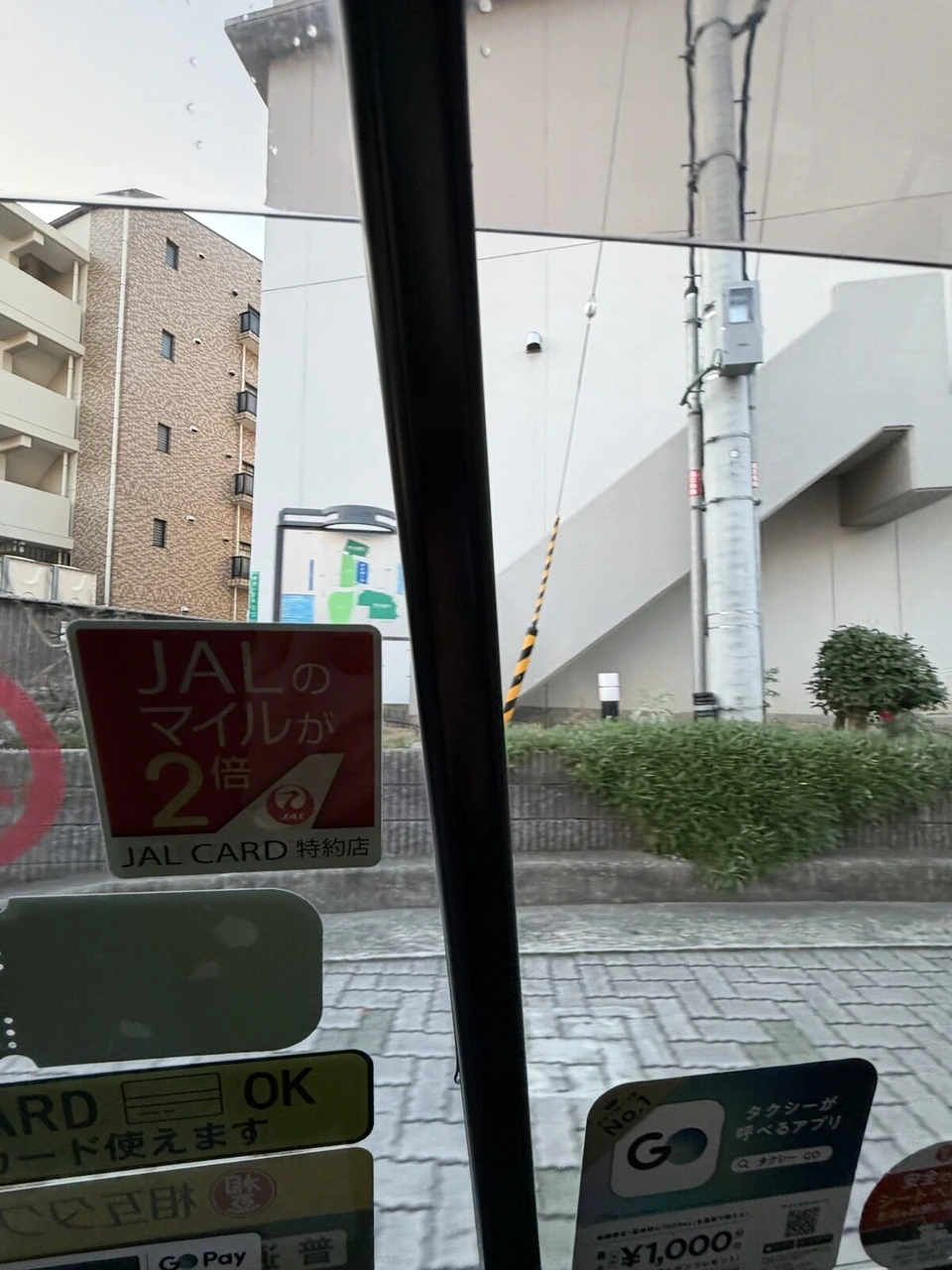 タクシーの窓越しに見た伊丹空港近くの建物。窓にJALカード特約店のステッカー