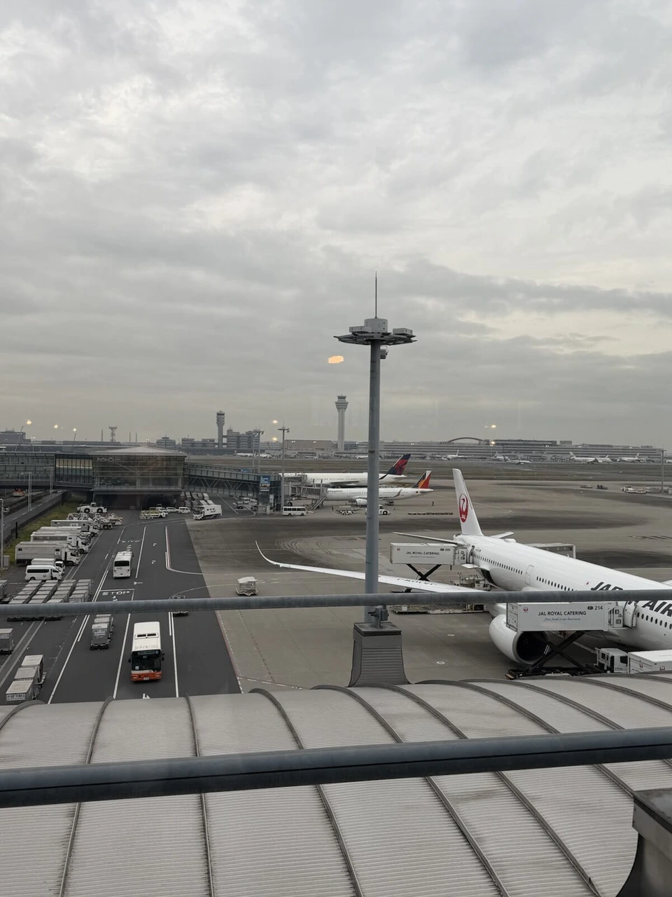 羽田のJALラウンジの窓から見た駐機中のJAL機とケータリング車、奥に管制塔