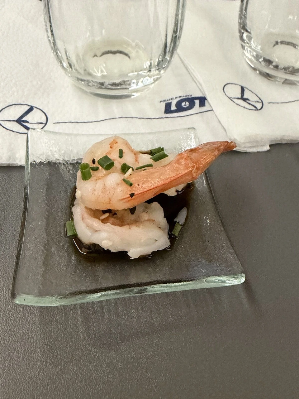 ガラスの小皿にのったエビの前菜。小ねぎとごまがかかり、後ろにLOTのナプキンとグラス