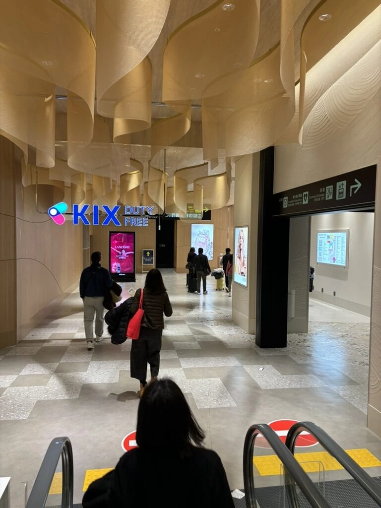 関西空港第1ターミナルの保安検査後の通路。KIX DUTY FREEの看板と波打つ木の天井