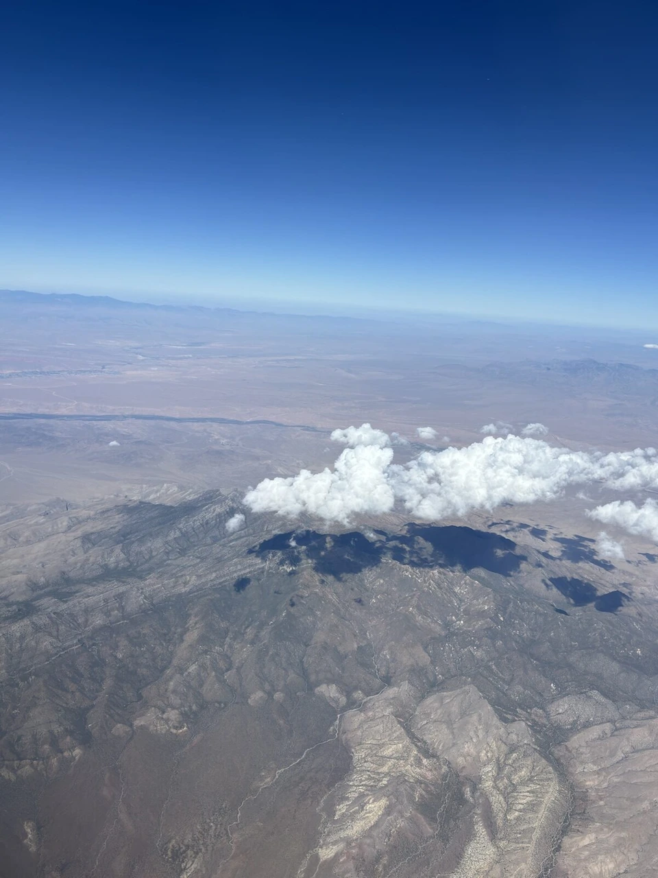 機窓から見た山並みと白い雲、乾いた大地