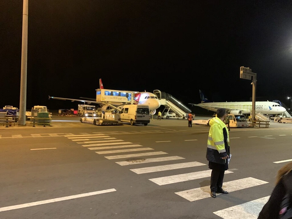 夜の駐機場。地上係員が立つ横断歩道の先に、照らされた飛行機とタラップ