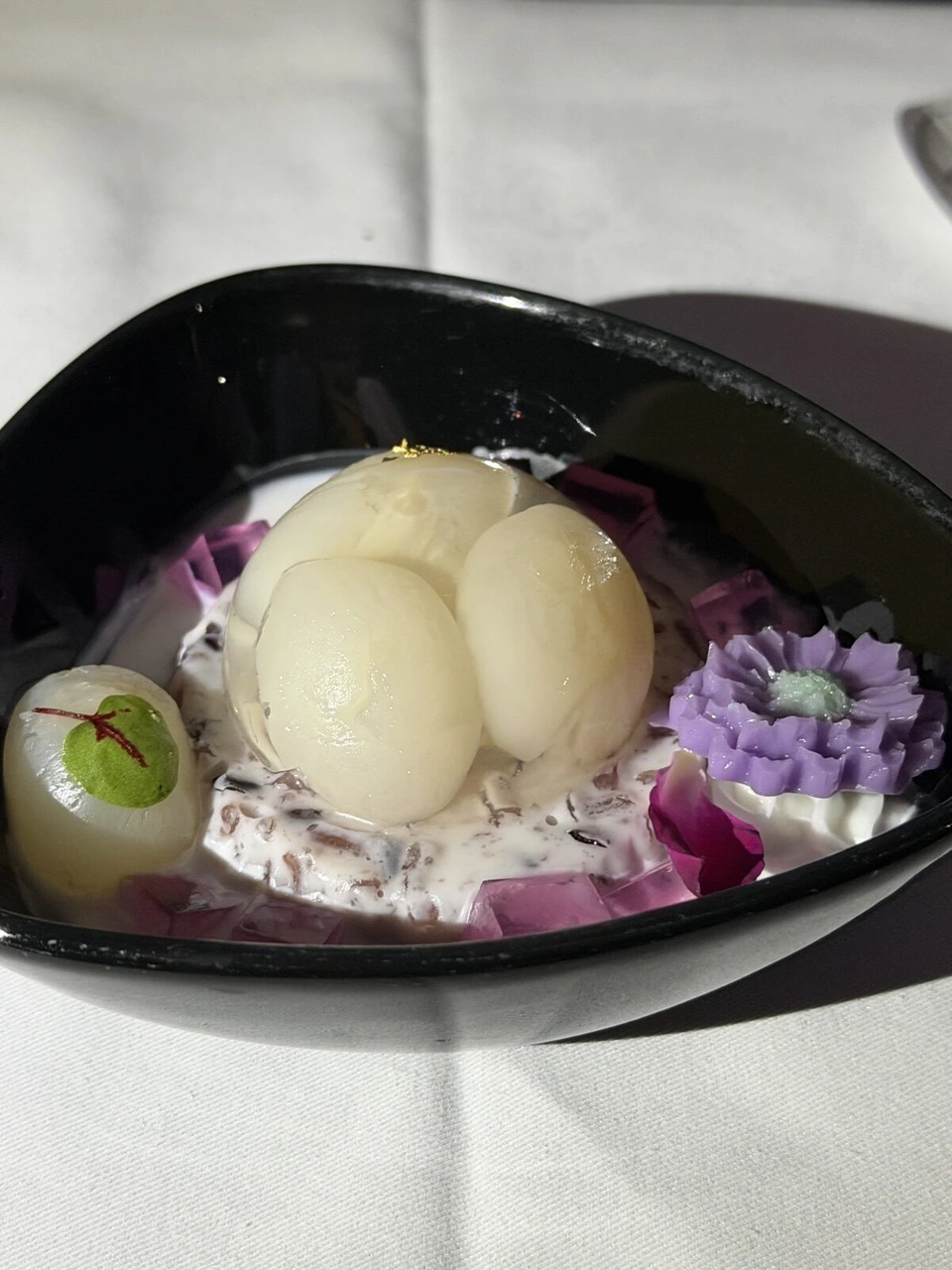 黒い器に入った白い果物のデザートと紫の花の飾り
