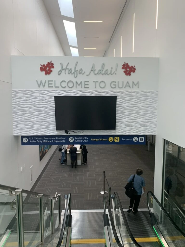 グアム空港の到着通路。Håfa Adai! WELCOME TO GUAMの看板とエスカレーター