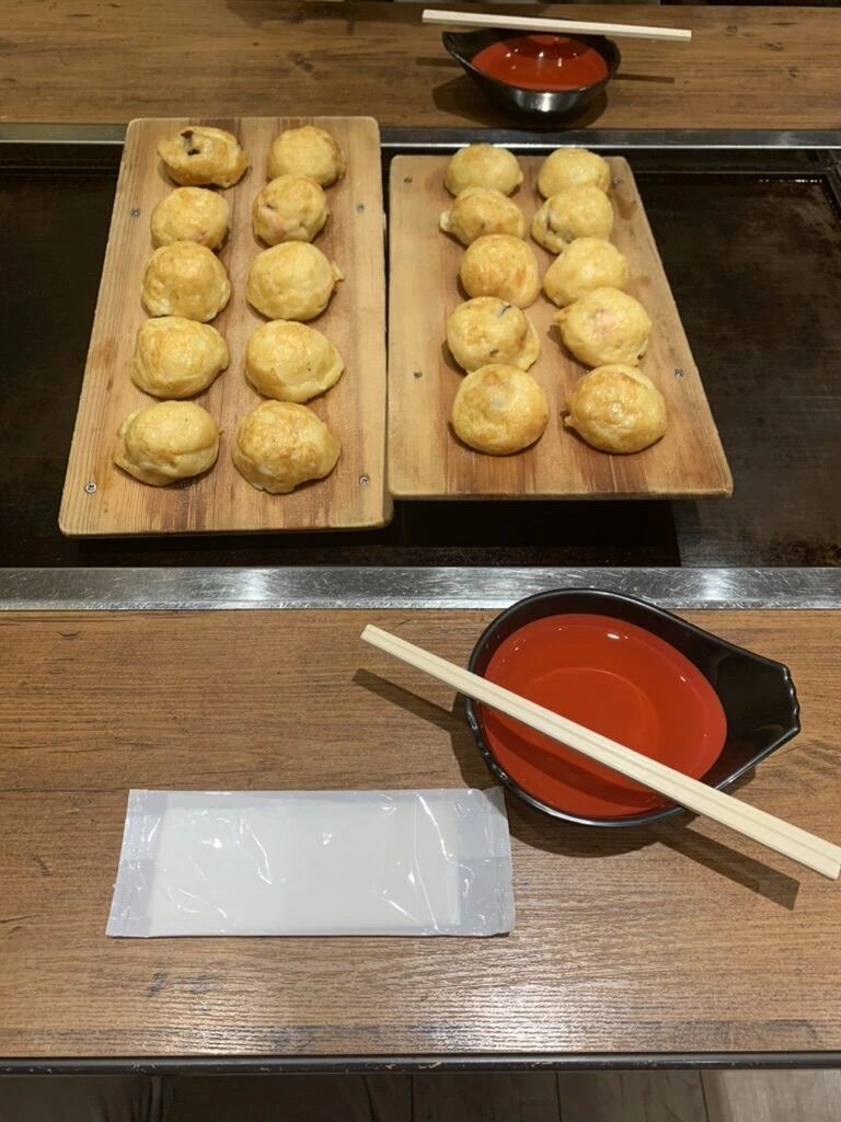 板に並んだ明石焼(玉子焼)と、だしの入った赤い器、箸とおしぼり