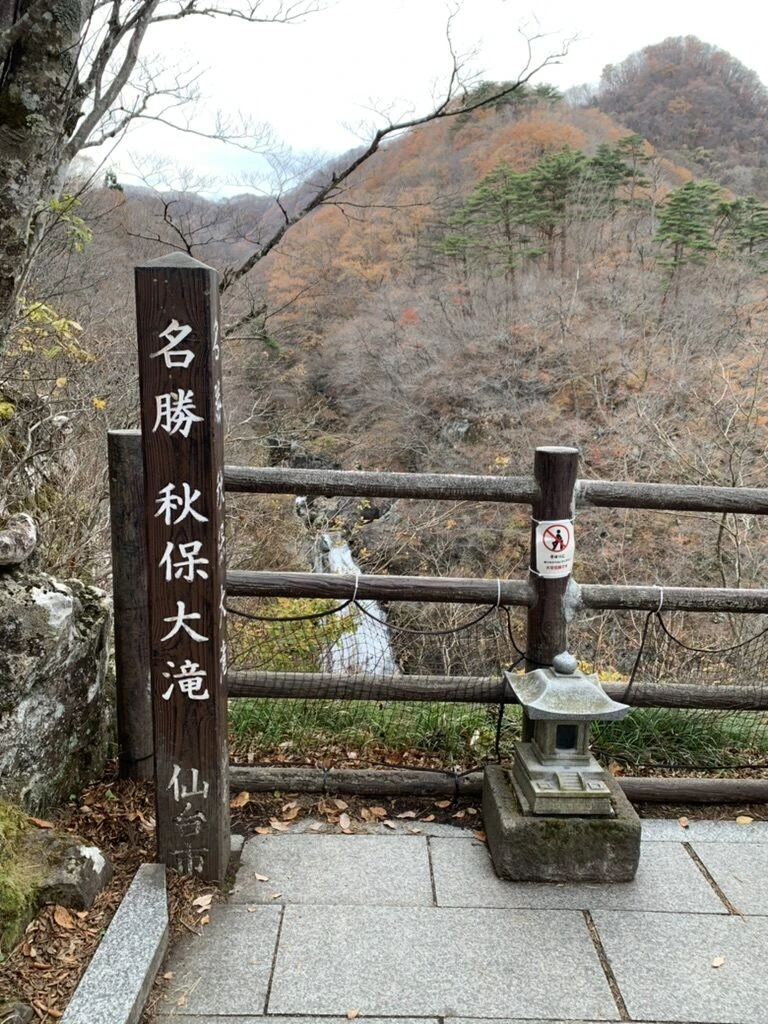 「名勝 秋保大滝」の標柱と柵、その奥の谷に流れ落ちる滝