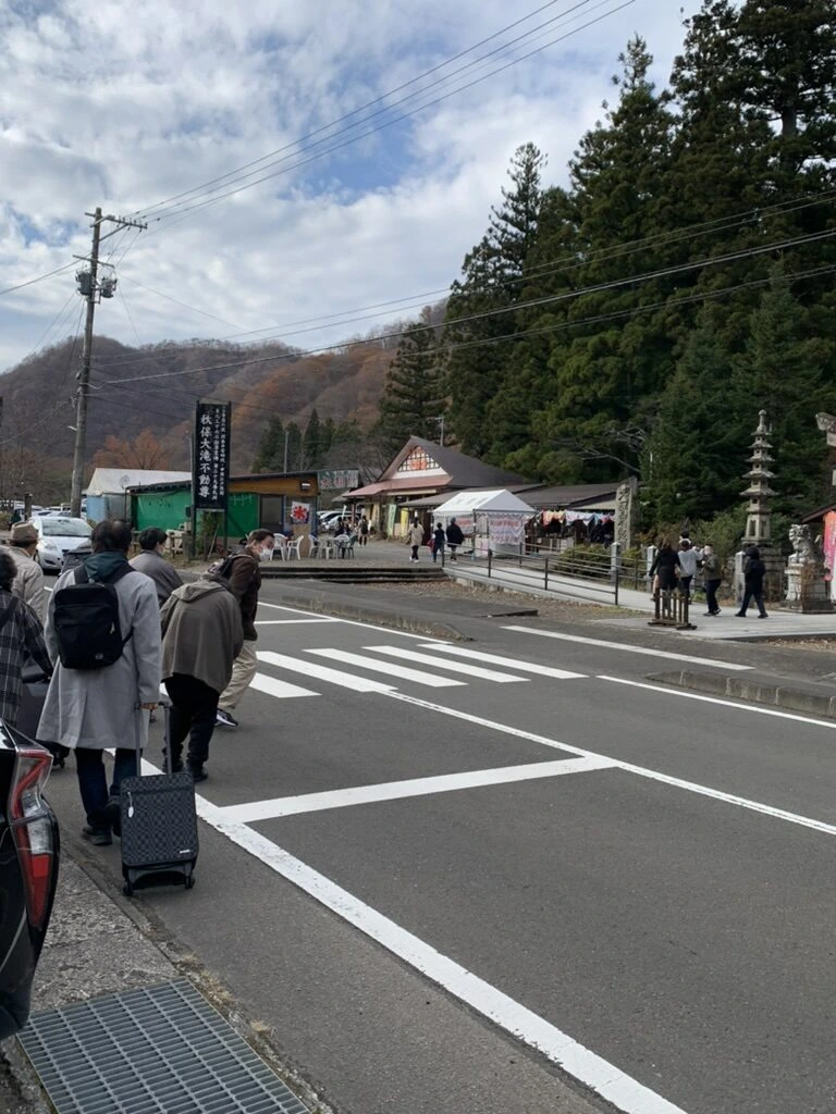 秋保大滝の入口付近の道路。紅葉の山と、歩く観光客の後ろ姿