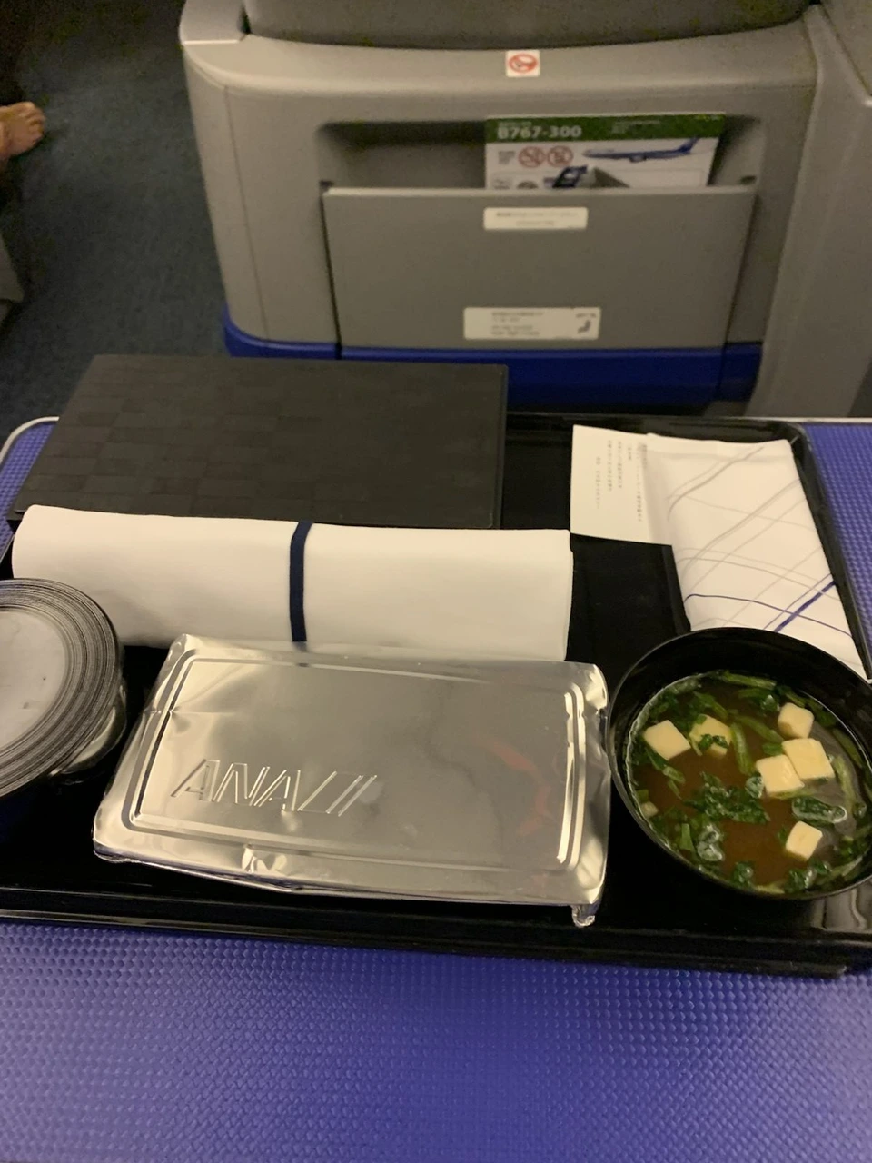 NH478のプレミアムクラスの座席テーブルに置かれた夕食の弁当とみそ汁。前の座席のポケットにB767-300の案内