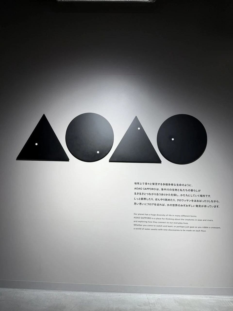 AOAO SAPPOROの白い壁に描かれた、三角と丸を組み合わせたロゴと説明文