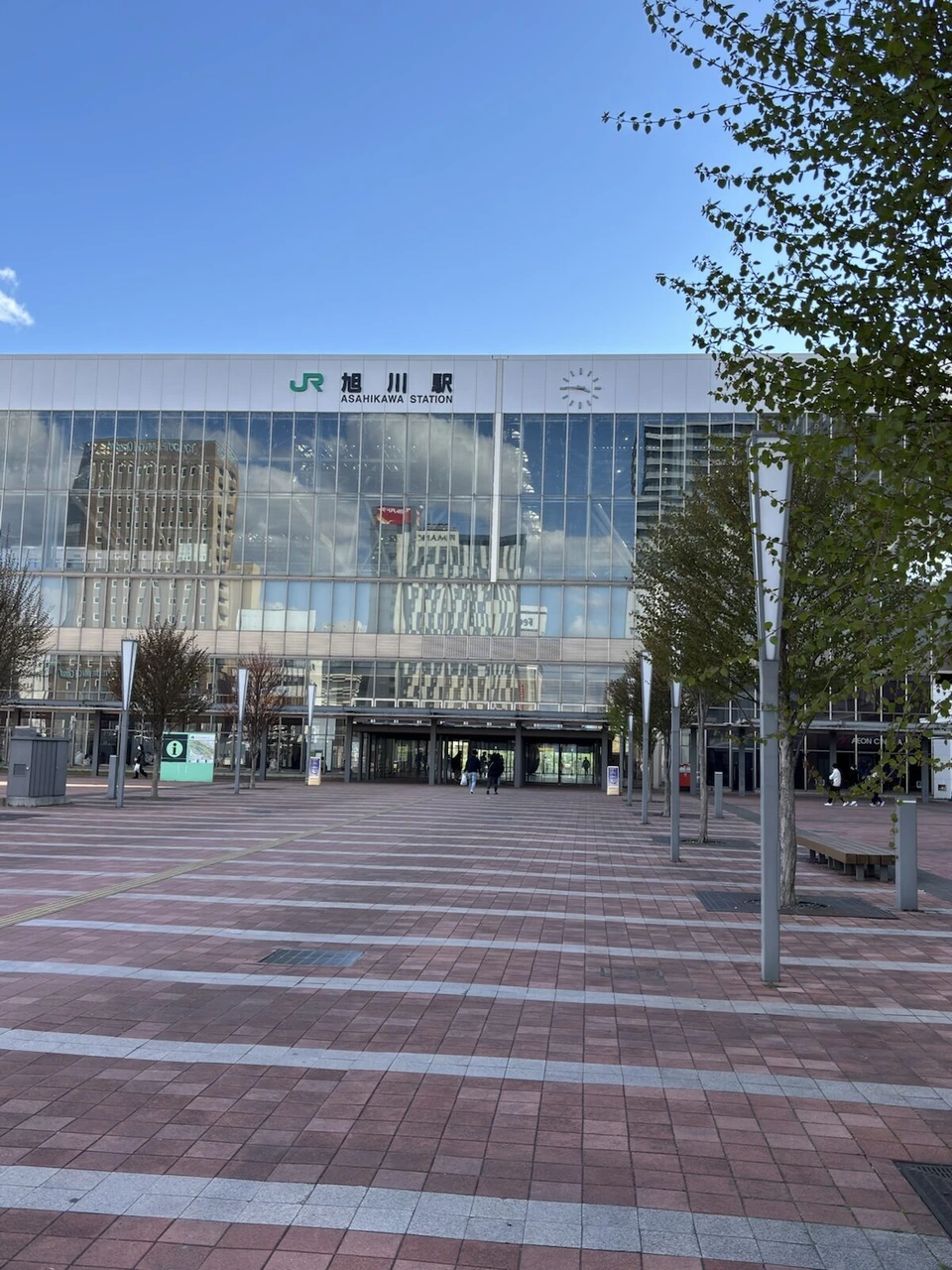 青空の下の旭川駅。ガラス張りの駅舎と広い駅前広場