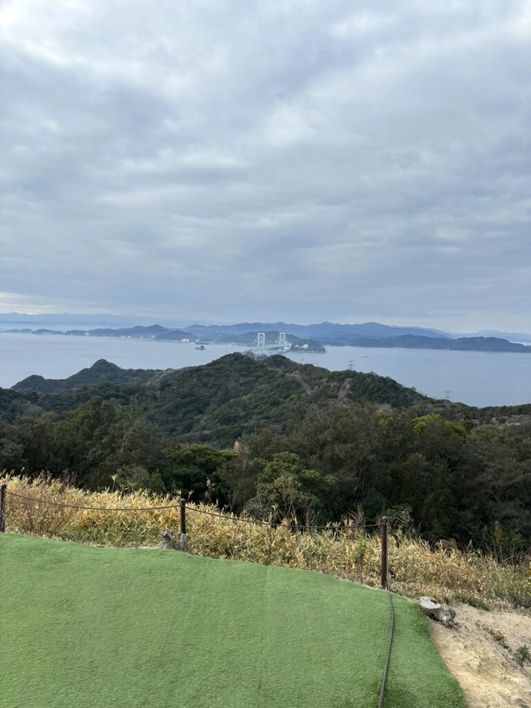 うずの丘の人工芝の展望スペースと、その先の山と海