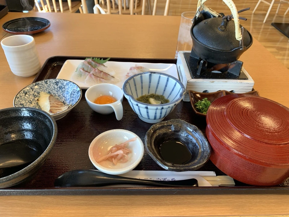 2023年1月の鯛の御膳。鯛の刺身、卵黄、わかめの小鉢、鉄瓶、赤いふた付きのお椀。箸袋に「うずの丘」