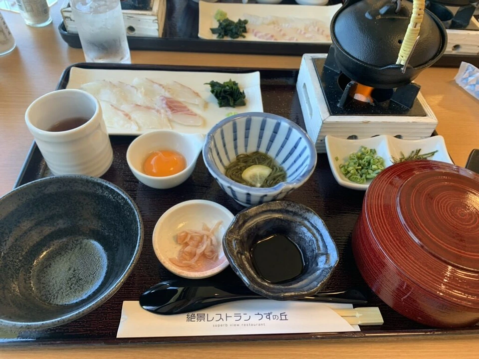 絶景レストラン うずの丘の鯛の御膳。鯛の刺身、卵黄、わかめの小鉢、醤油、鉄瓶をのせた小さなコンロ、赤いふた付きのお椀。箸袋に店名