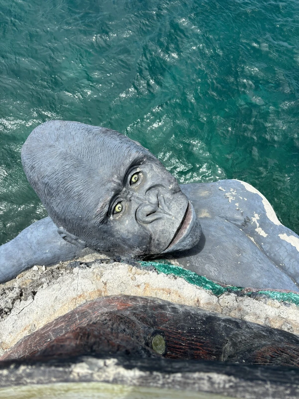 海の上の岩に寝そべる灰色のゴリラのような像
