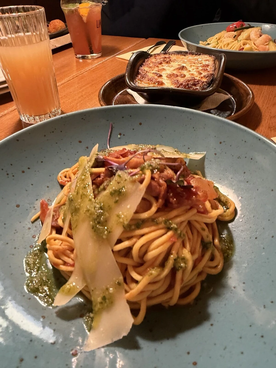 青い皿に盛られたトマトソースのパスタと、奥のグラタン、オレンジのジュース