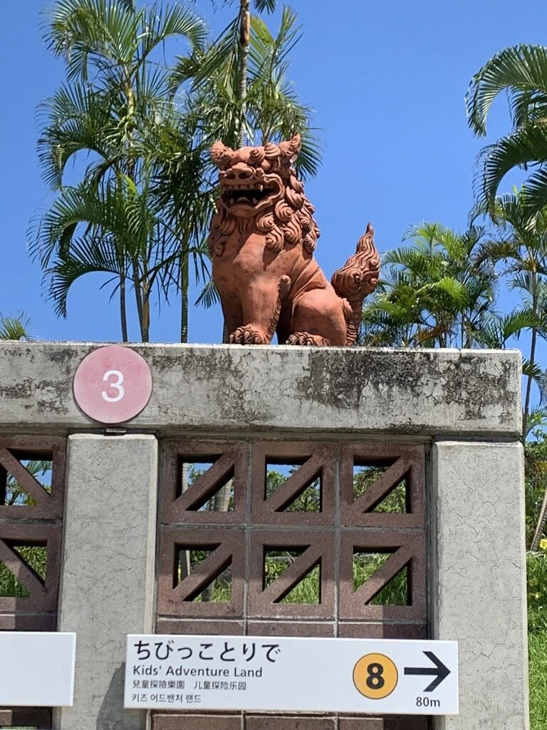 海洋博公園の塀の上の赤いシーサーと、ちびっこ・ランド方面を示す番号つきの案内板