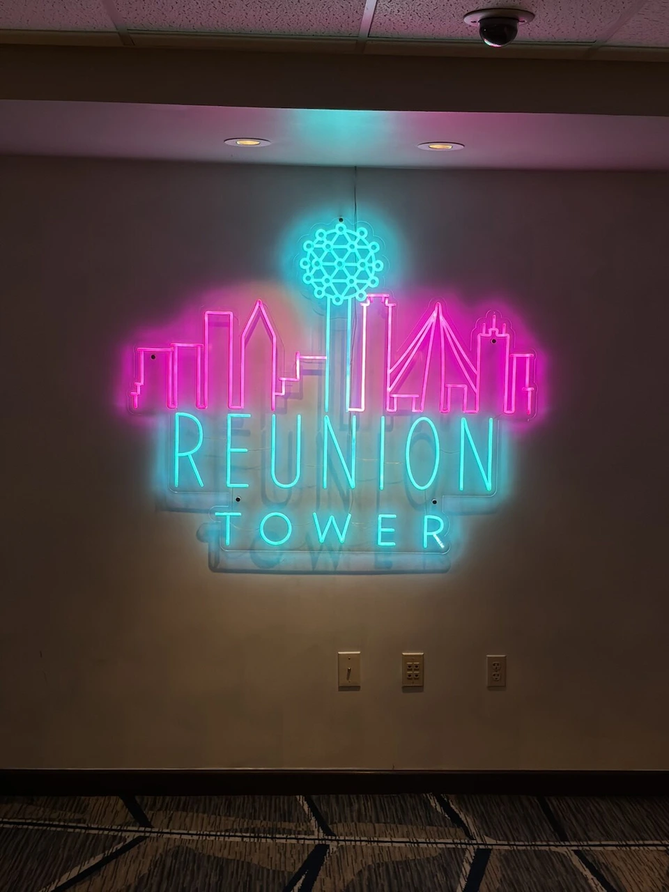 リユニオンタワーの入口の壁に光るピンクと水色のネオンサイン。ダラスのビル群の絵とREUNION TOWERの文字