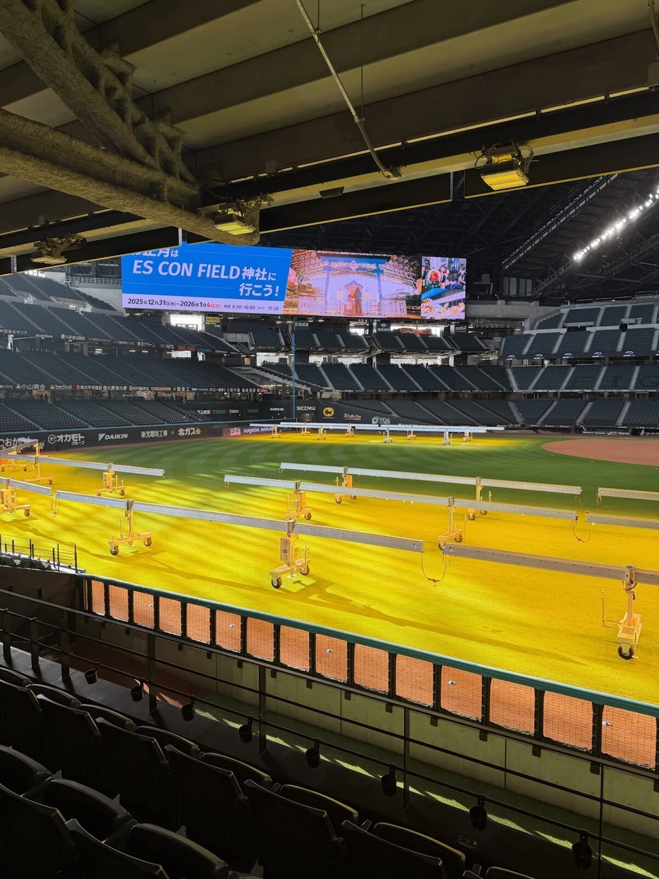 エスコンフィールドHOKKAIDOのスタンドから見たフィールド。芝生に黄色いライト、大型ビジョンにES CON FIELD神社の告知
