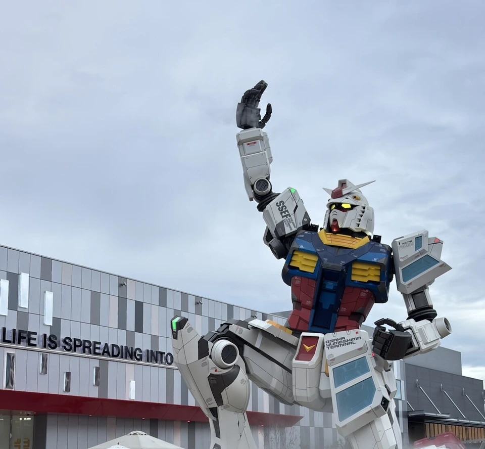 GUNDAM NEXT FUTURE PAVILIONの、片手を空に上げ片ひざをついた実物大ガンダム像。肩にSSEF、腰にOSAKA YUMESHIMA TERMINALの文字