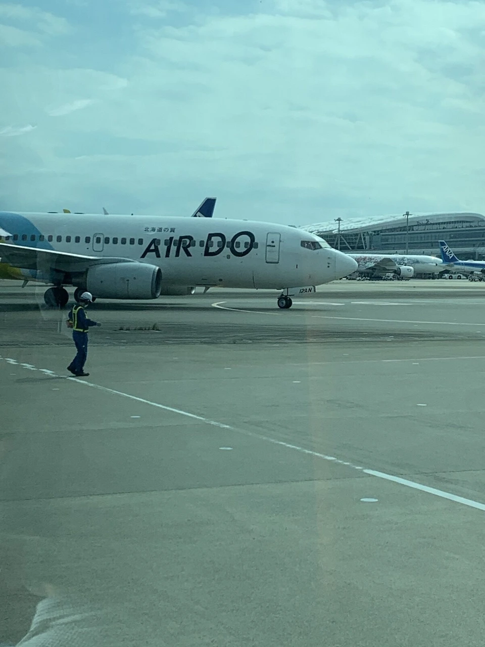 駐機場で誘導の合図を出す係員と、その奥をゆっくり進むAIRDOのボーイング737