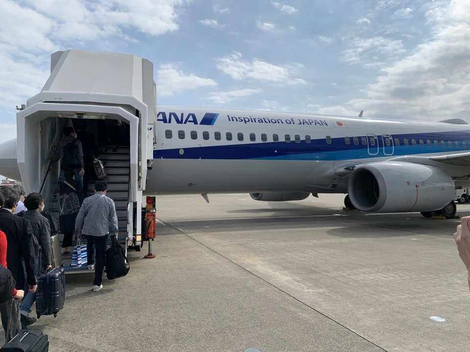 ANAのボーイング737-800の前方ドアに付けられた白いタラップ車と、階段を上る乗客