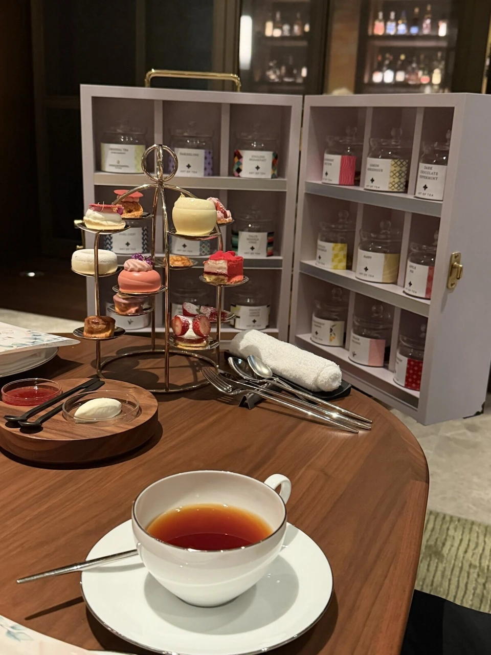 紅茶の缶が並んだ白い箱の前に、金色の細いスタンドにのったいちごのスイーツと紅茶のカップ