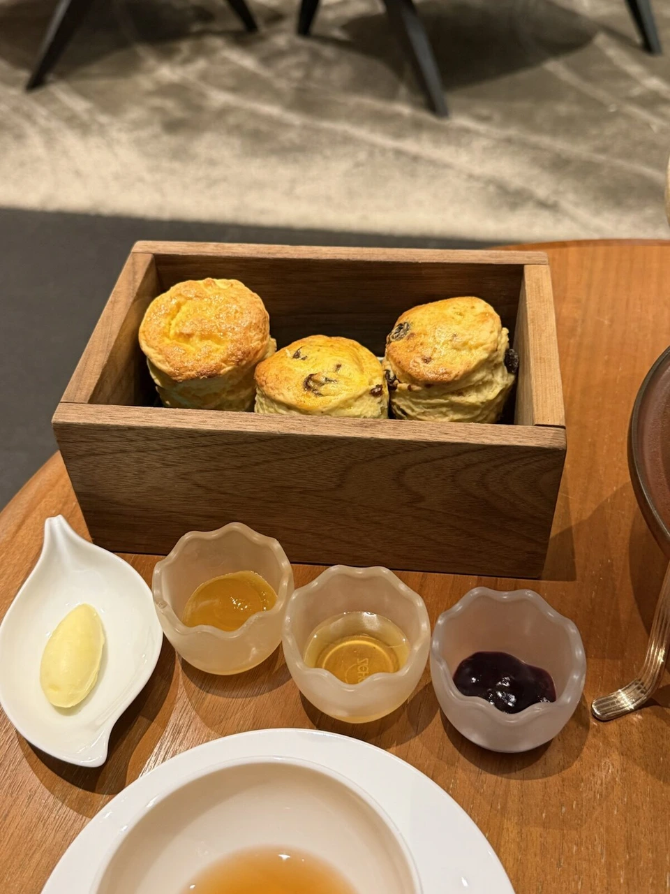 木の箱に入ったスコーン3個と、バター、2種類のはちみつ、ベリーのジャムの小皿