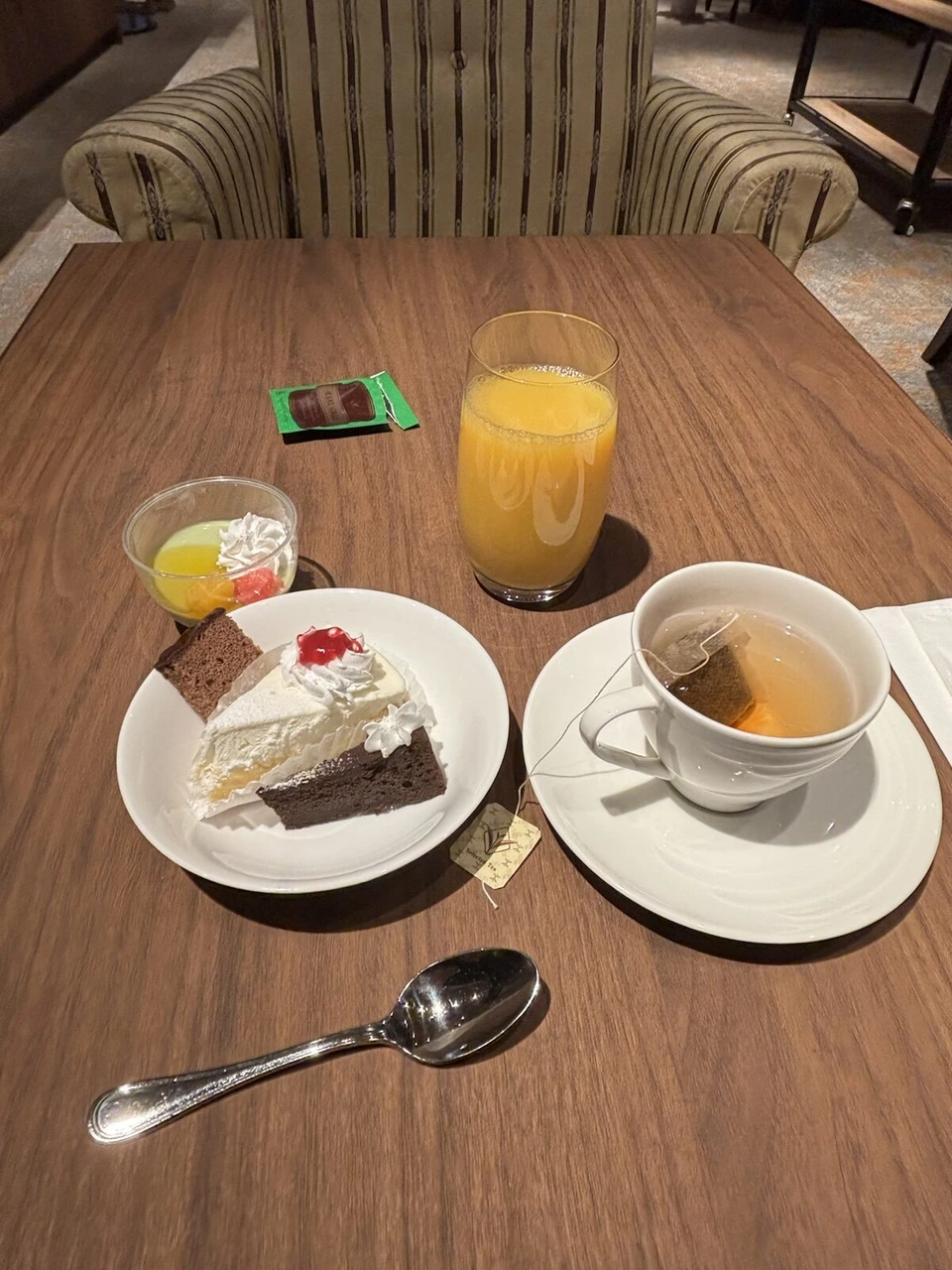 ラウンジのテーブルにケーキの皿、紅茶のカップ、オレンジジュース、小さなゼリー
