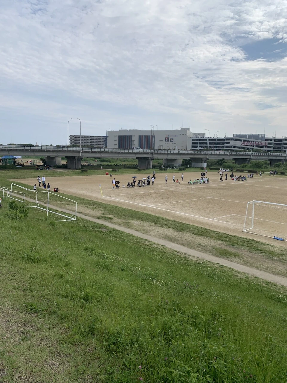 空港の近くの河川敷。手前に草の土手と土のグラウンド、奥の堤防の向こうに伊丹空港のターミナルビル