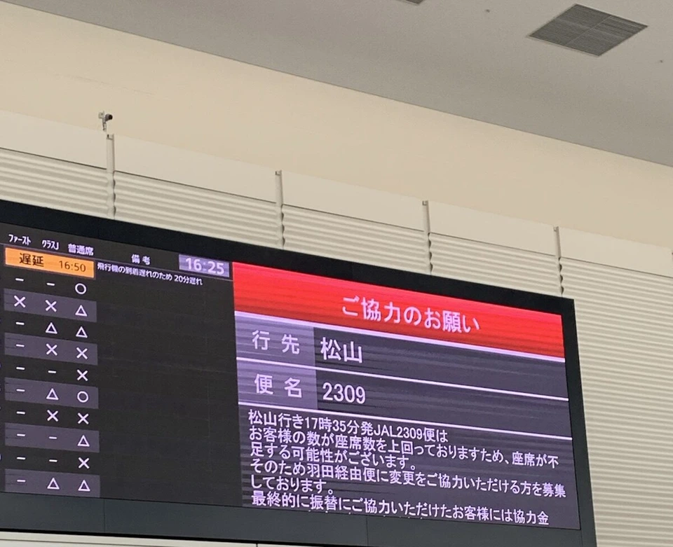 伊丹空港のJALカウンターの上の大きな案内表示。赤い見出しで「ご協力のお願い」、行先は松山、便名は2309と出ている