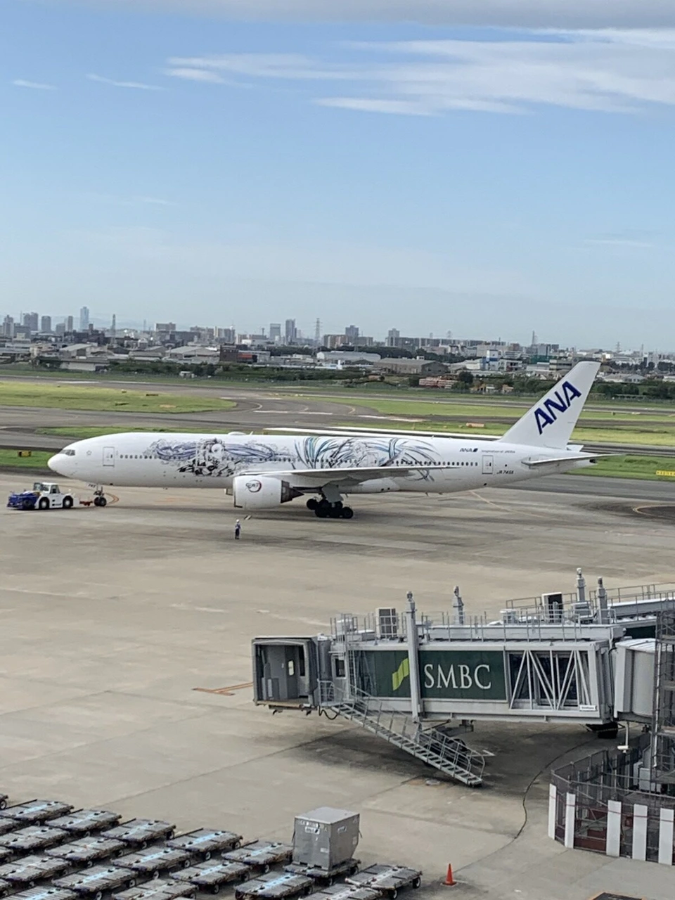 朝の伊丹空港で、白い機体にスター・ウォーズのキャラクターが線で描かれたANA機が、車に引かれて地上を動いている。手前に搭乗橋
