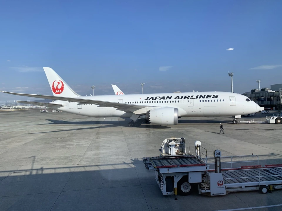 朝の伊丹空港の駐機場に止まるJALのボーイング787。手前に荷物を運ぶ白い車両