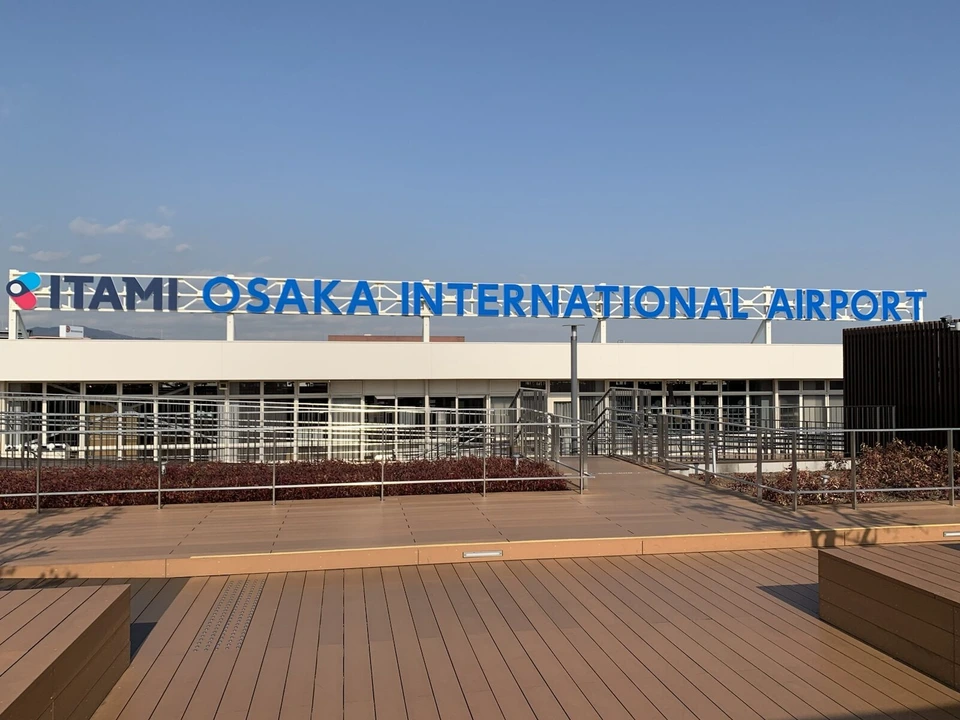 冬の晴れた日の伊丹空港の屋上展望デッキ。手前に茶色のウッドデッキ、奥のターミナルの屋根に青い「ITAMI OSAKA INTERNATIONAL AIRPORT」の文字