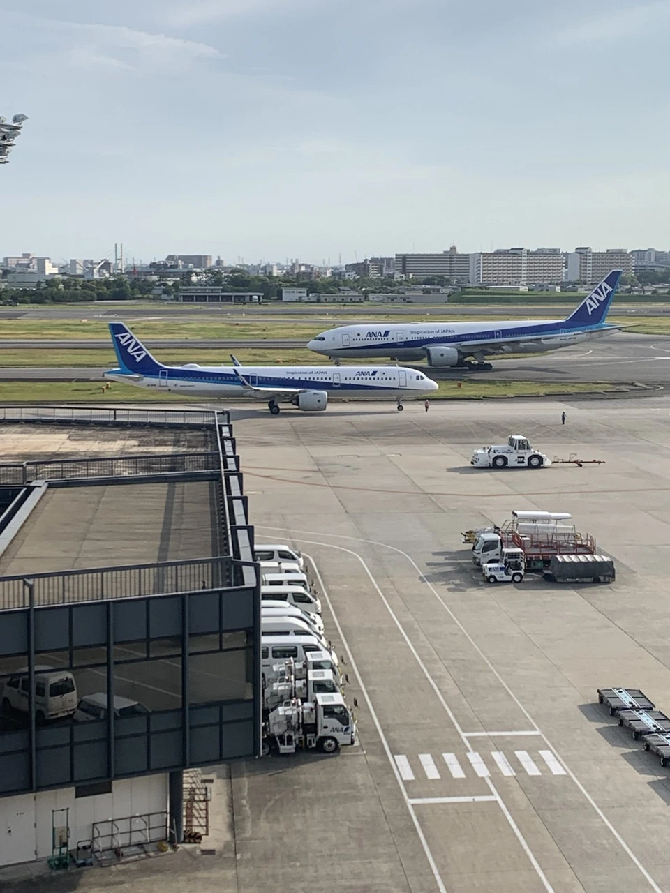 伊丹空港の屋上展望デッキから見た、誘導路を進むANAの2機。手前に駐機場と地上の車両
