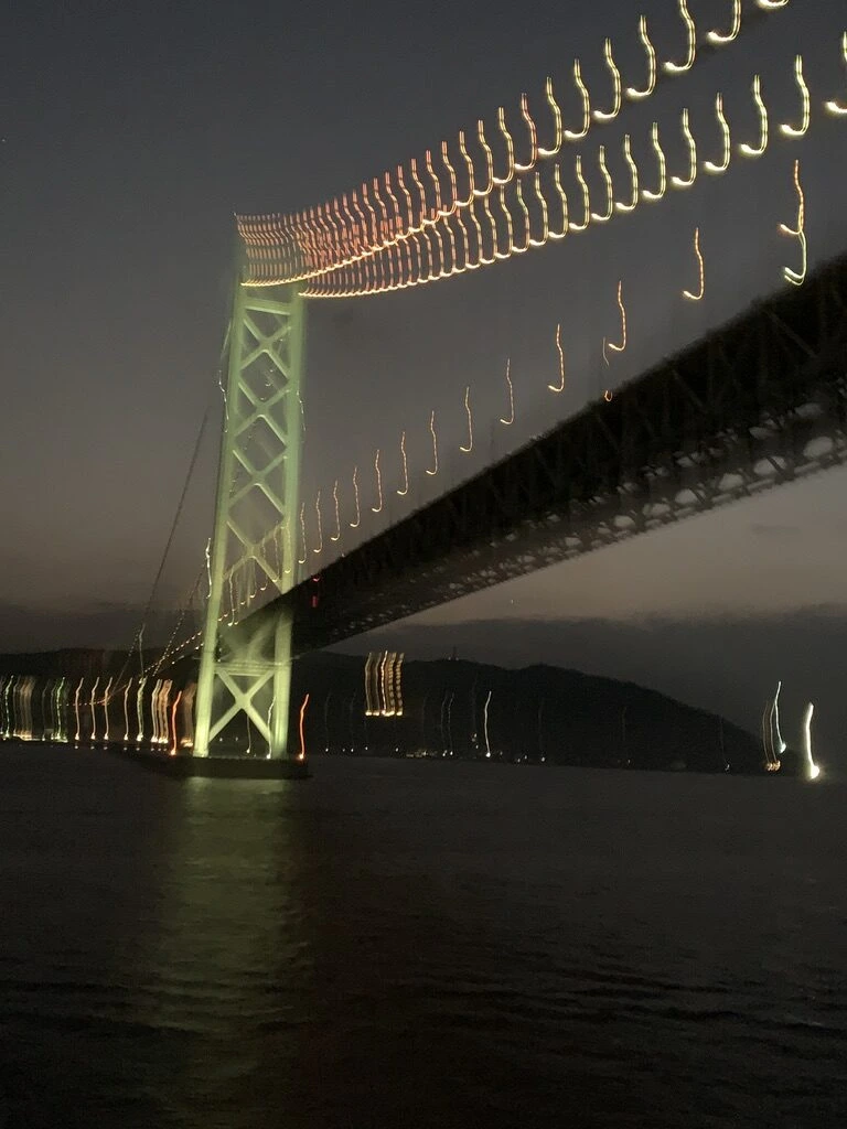 船の揺れで光が線状に流れた、明石海峡大橋の主塔とケーブルの夜景