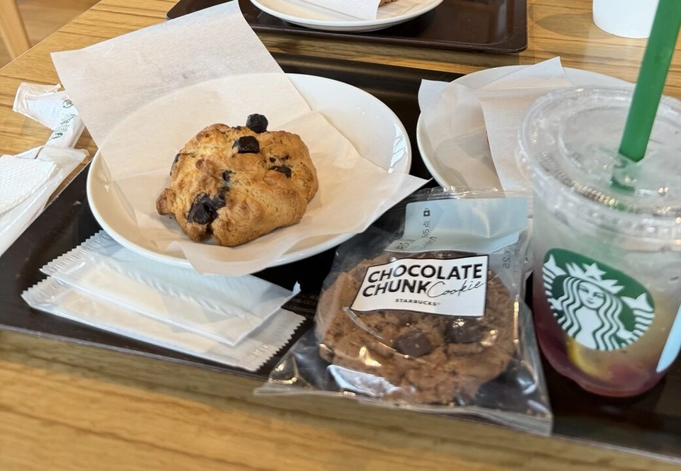 スターバックスのトレーにのった黒い粒入りのスコーン、袋入りのチョコレートチャンククッキー、赤紫色のアイスドリンク