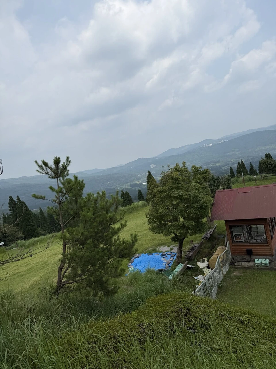 霧島神話の里公園のリフトの上から見た景色。赤い屋根の小屋と松の木、その奥に霧島の山々