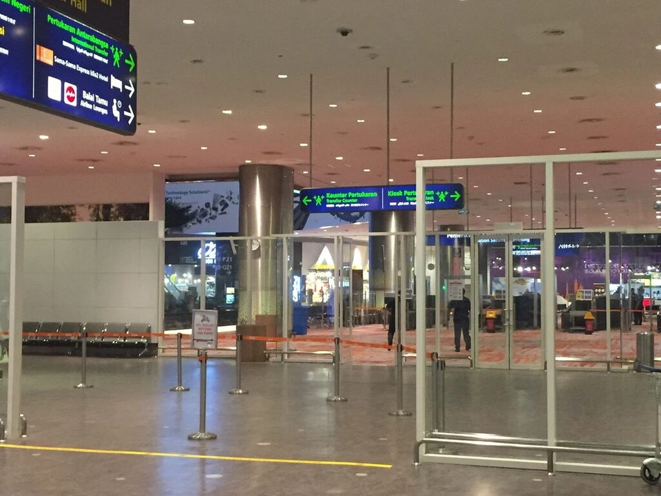 夜のクアラルンプール空港KLIA2の到着エリア。ガラスの仕切りと案内板、人はまばら
