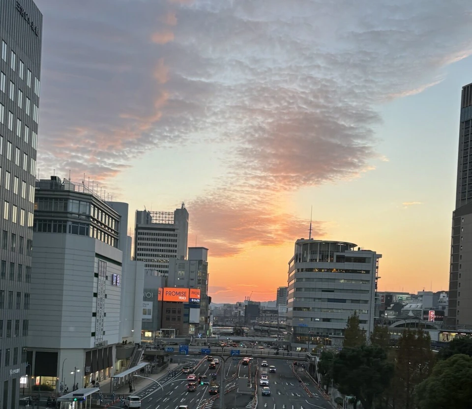三宮の高いところから見た夕焼け。ビルの間の空がオレンジとピンクに染まり、下に大通りと車の列