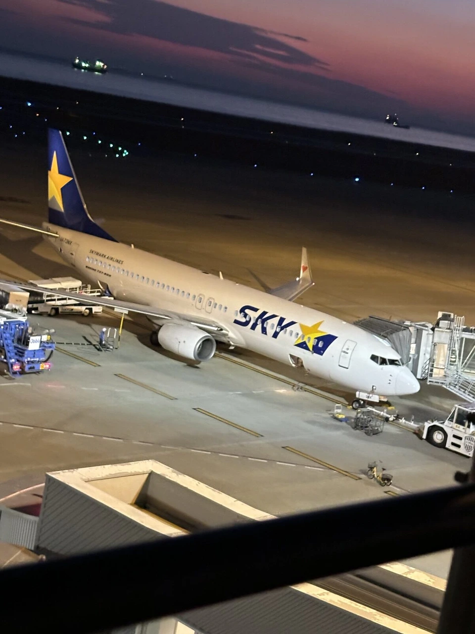 夕暮れの神戸空港。屋上展望デッキから見下ろした搭乗橋につながるスカイマークのボーイング737。奥の海の上の空がピンク色に染まっている