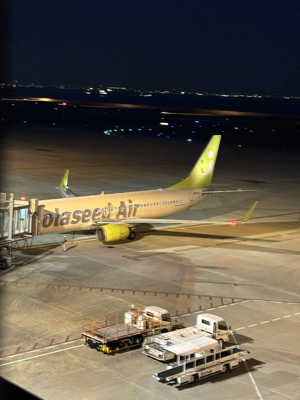 夜の神戸空港の駐機場で、ライトに照らされたソラシドエアのボーイング737。黄緑色の尾翼とエンジン、奥に暗い海